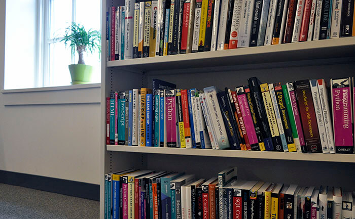 Bookshelf in the Caktus office with 3 shelves full of various books on web development and other technical topics