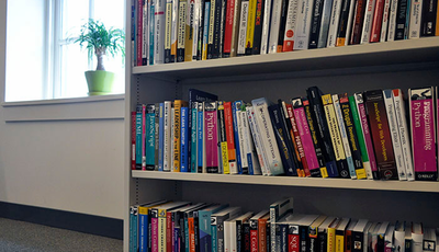 Bookshelf in the Caktus office with 3 shelves full of various books on web development and other technical topics